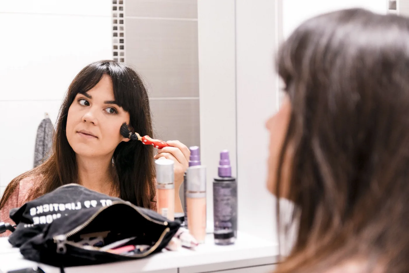 žena si nanáší make-up štětcem před zrcadlem